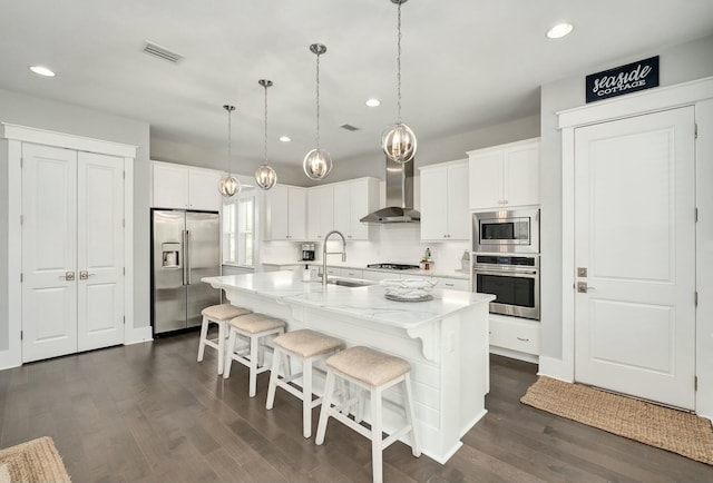 kitchen featuring visible vents, dark wood finished floors, a sink, stainless steel appliances, and wall chimney exhaust hood