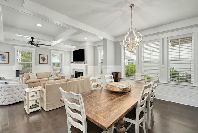 dining room featuring wainscoting, beamed ceiling, ceiling fan with notable chandelier, dark wood-style floors, and a glass covered fireplace
