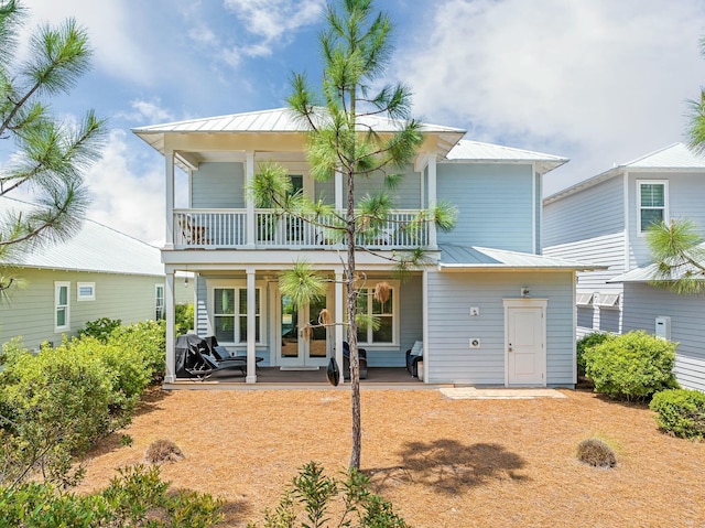 rear view of property featuring covered porch, metal roof, french doors, and a balcony