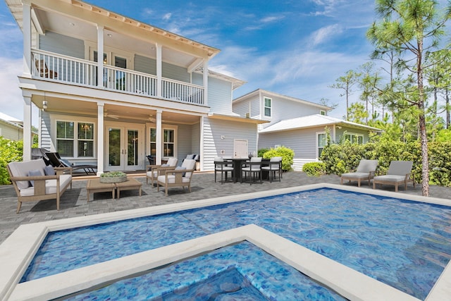 back of property featuring a hot tub, a covered pool, ceiling fan, a balcony, and french doors