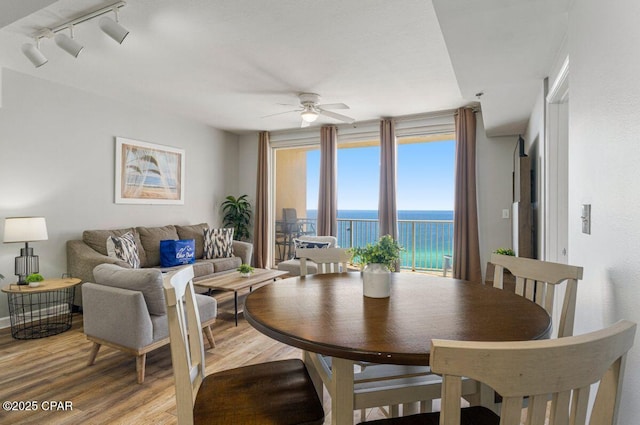 dining area featuring rail lighting, a water view, wood finished floors, and ceiling fan