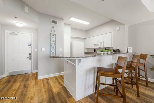 kitchen with stone countertops, a peninsula, white appliances, visible vents, and white cabinets