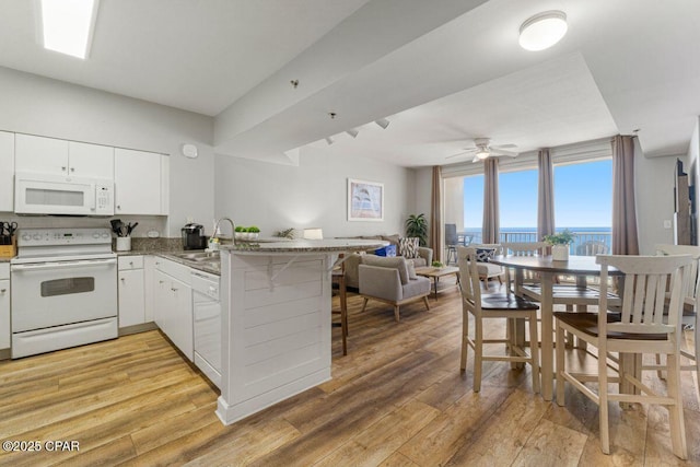 kitchen featuring a sink, a peninsula, white appliances, open floor plan, and white cabinets