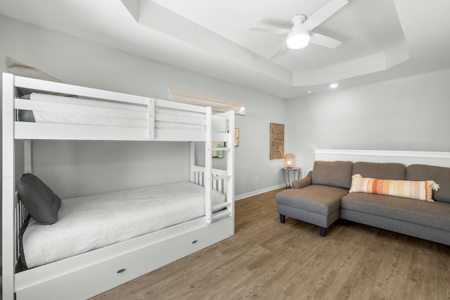 bedroom featuring baseboards, a ceiling fan, a tray ceiling, and wood finished floors
