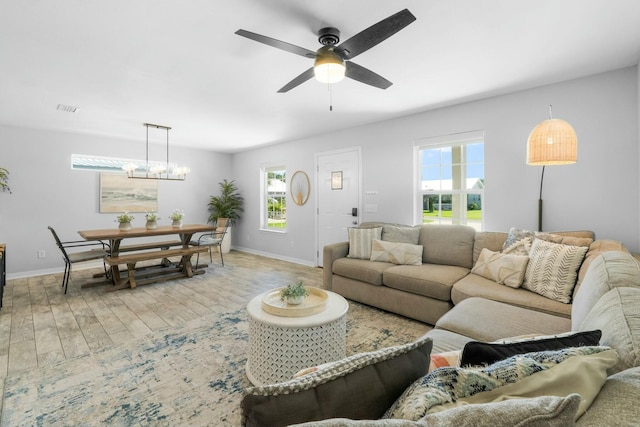 living area featuring baseboards, ceiling fan with notable chandelier, light wood finished floors, and a wealth of natural light