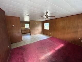 unfurnished living room featuring healthy amount of natural light, wooden walls, and ceiling fan