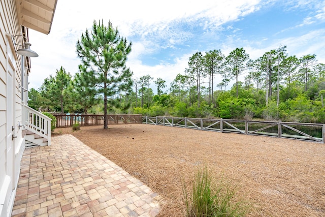 view of yard with fence, view of wooded area, and a patio