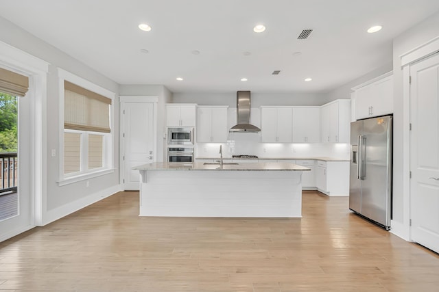 kitchen with stainless steel appliances, wall chimney exhaust hood, a sink, white cabinets, and recessed lighting