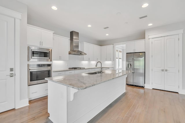 kitchen featuring appliances with stainless steel finishes, wall chimney exhaust hood, a sink, light wood-style flooring, and white cabinets