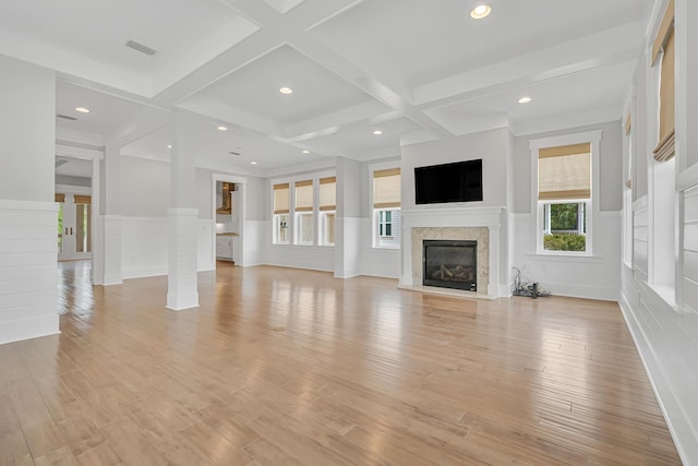 unfurnished living room featuring a wainscoted wall, coffered ceiling, light wood-type flooring, beamed ceiling, and a glass covered fireplace
