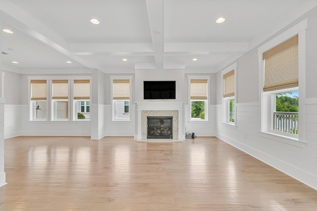 unfurnished living room featuring a high end fireplace, a wainscoted wall, recessed lighting, beam ceiling, and light wood finished floors