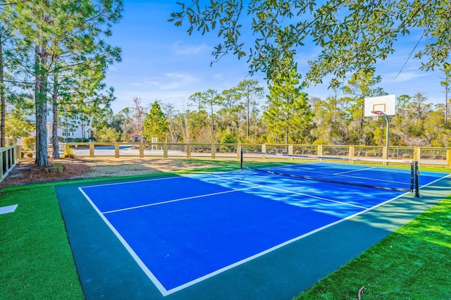 view of sport court featuring a tennis court, fence, and view of wooded area