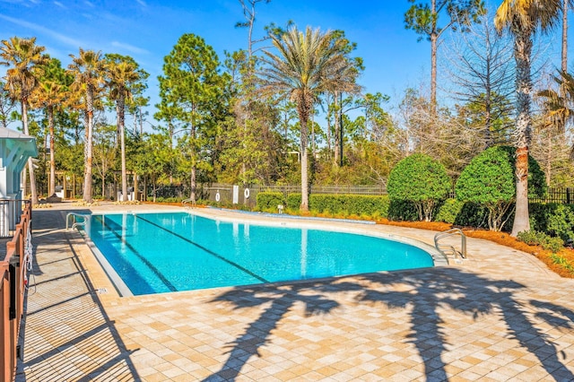 community pool featuring fence, a patio, and view of wooded area