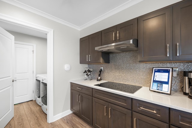 kitchen featuring washing machine and dryer, light wood-type flooring, dark brown cabinets, black electric stovetop, and under cabinet range hood