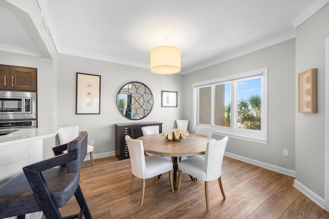dining area with baseboards, ornamental molding, and light wood-style floors