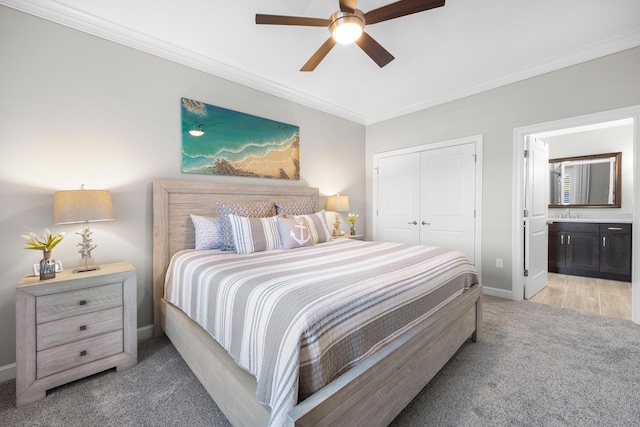 bedroom featuring a closet, ornamental molding, baseboards, light colored carpet, and ensuite bath