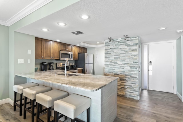 291 Scenic Gulf Dr Unit 900, Miramar Beach, FL 32550 - kitchen featuring stainless steel appliances, crown molding, brown cabinets, a sink, and a peninsula