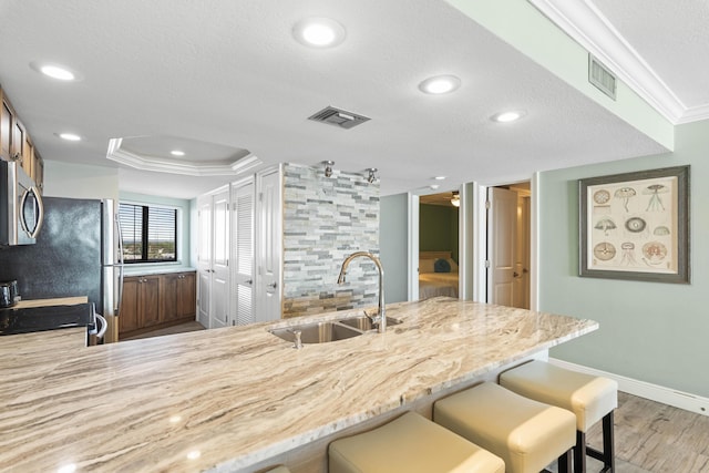 291 Scenic Gulf Dr Unit 900, Miramar Beach, FL 32550 - kitchen featuring stainless steel microwave, a sink, a breakfast bar area, wood finished floors, and light stone counters