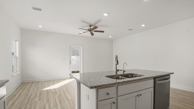 kitchen featuring dishwasher, light stone countertops, light wood-type flooring, and a sink