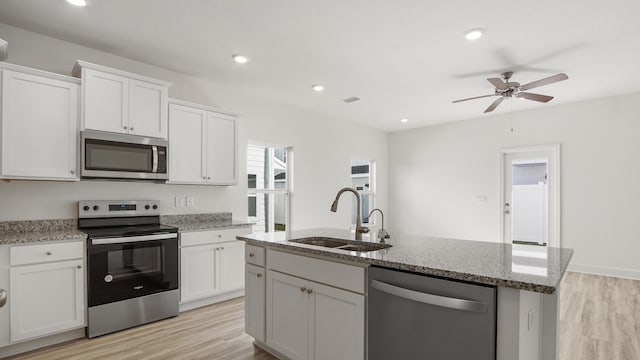 kitchen featuring light wood finished floors, stainless steel appliances, white cabinets, and a sink