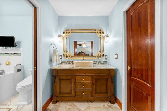 bathroom featuring toilet, baseboards, marble look tiles, and vanity