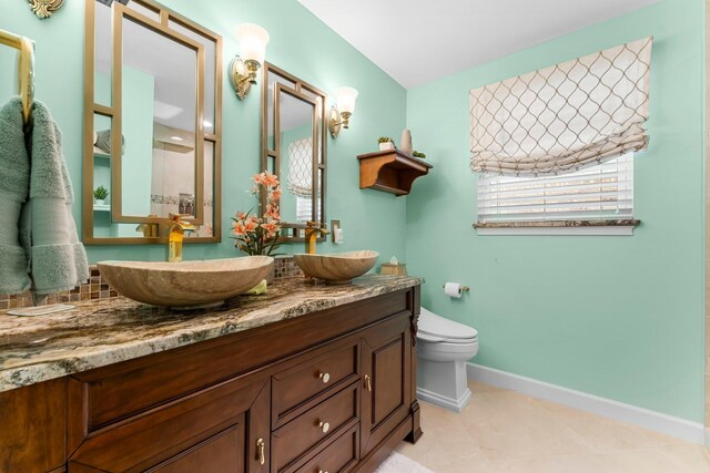 bathroom with baseboards, double vanity, toilet, and tile patterned floors