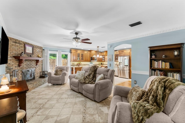 living area with ceiling fan, ornamental molding, arched walkways, and a brick fireplace