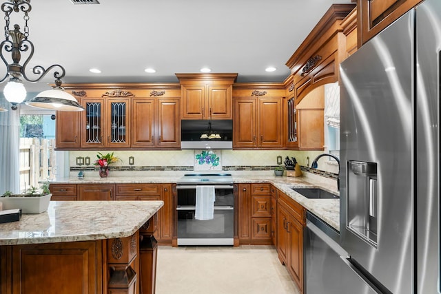 kitchen featuring stainless steel appliances, a sink, brown cabinets, light stone countertops, and recessed lighting