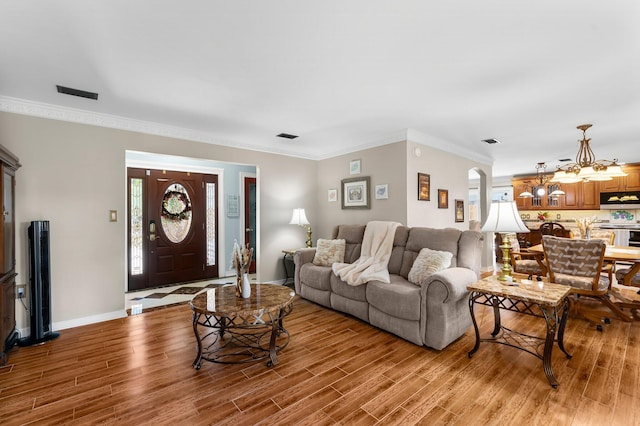 living room featuring light wood finished floors, a chandelier, crown molding, healthy amount of natural light, and baseboards