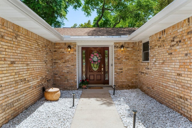 view of exterior entry featuring brick siding and roof with shingles