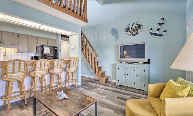 living room with a towering ceiling, wood finished floors, stairs, and baseboards