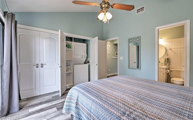 bedroom featuring stacked washer / drying machine, wood finished floors, visible vents, a closet, and high vaulted ceiling