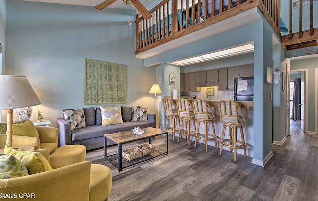 living room featuring ceiling fan, baseboards, dark wood-style flooring, and a towering ceiling