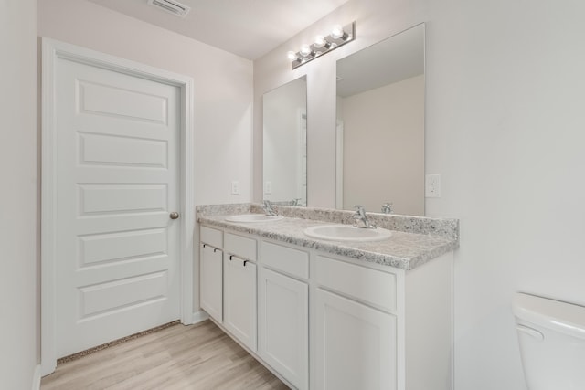 bathroom with visible vents, toilet, double vanity, and a sink