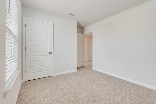 unfurnished bedroom featuring baseboards, visible vents, multiple windows, and carpet flooring