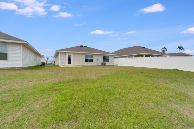 rear view of house with cooling unit, a lawn, and fence