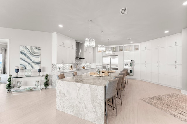 320 Harbor Blvd Unit 1201, Destin, FL 32541 - kitchen featuring visible vents, wall chimney range hood, white cabinets, light wood-style flooring, and appliances with stainless steel finishes