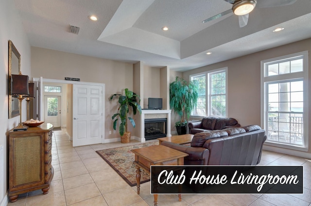 9124 Orlando Ave, Navarre, FL 32566 - living room featuring light tile patterned floors, ceiling fan, recessed lighting, a glass covered fireplace, and a tray ceiling