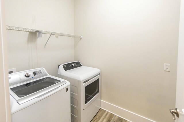 washroom featuring washing machine and clothes dryer, wood finished floors, laundry area, and baseboards