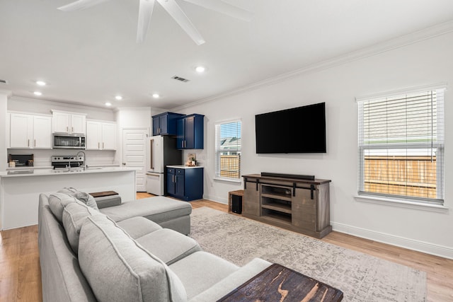 living room featuring crown molding, a ceiling fan, visible vents, and light wood-style flooring