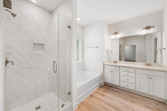 bathroom featuring wood finished floors, a shower stall, double vanity, a bath, and a sink