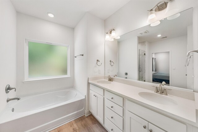 ensuite bathroom with wood finished floors, visible vents, a bath, and a sink