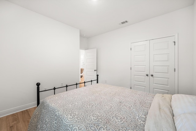 bedroom featuring wood finished floors, baseboards, visible vents, and a closet
