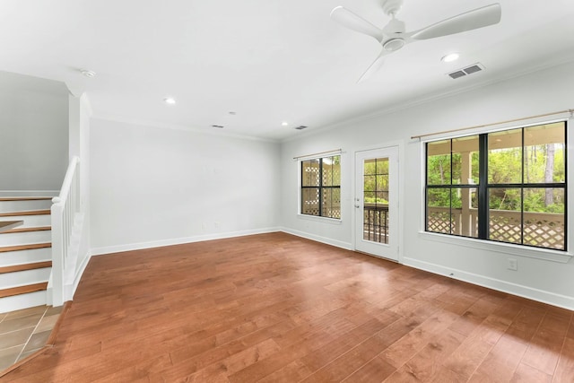 empty room featuring wood finished floors, stairway, ornamental molding, baseboards, and visible vents