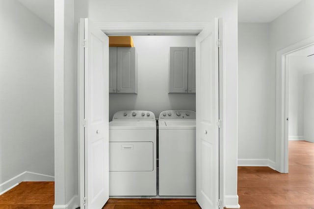 laundry room featuring wood finished floors, washer and clothes dryer, cabinet space, and baseboards