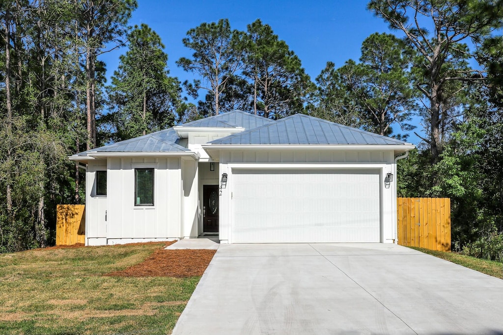 view of front of property featuring a garage, a standing seam roof, board and batten siding, metal roof, and driveway