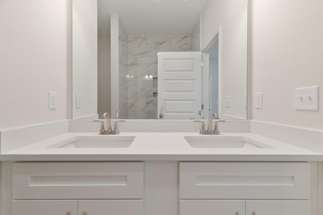 full bath with a marble finish shower, double vanity, and a sink