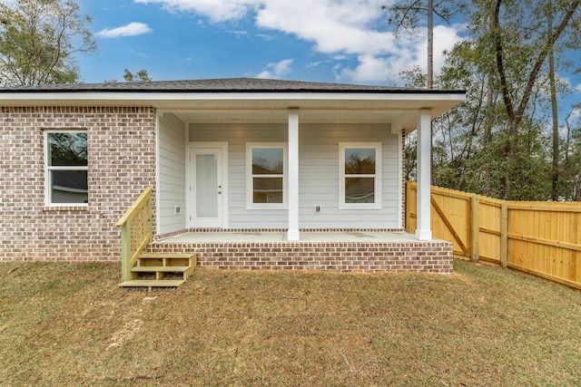 back of property with a porch, a lawn, brick siding, and fence