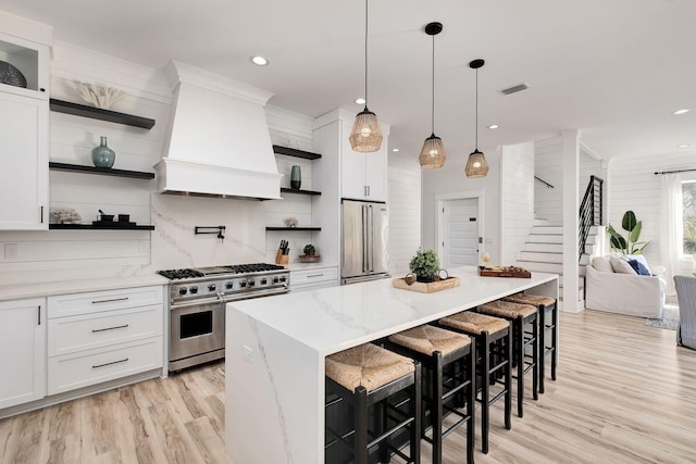 kitchen with high quality appliances, open shelves, custom range hood, light wood-style floors, and white cabinets