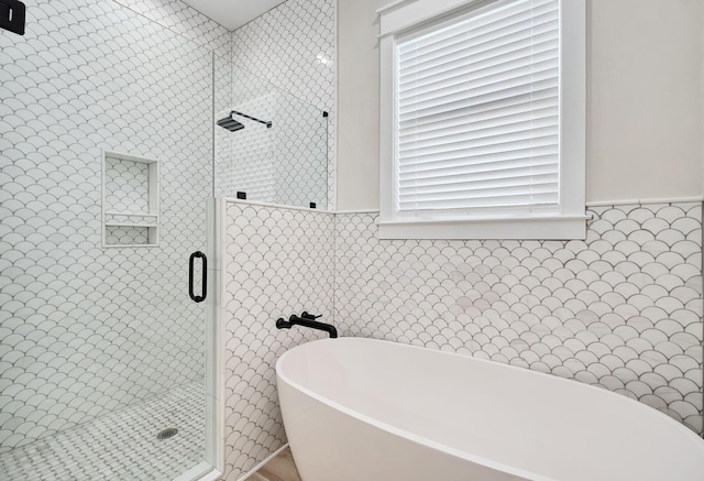 full bathroom with a stall shower, a freestanding bath, tile walls, and wainscoting